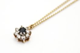 A yellow metal cluster pendant set with one round faceted sapphire and cubic zirconia,