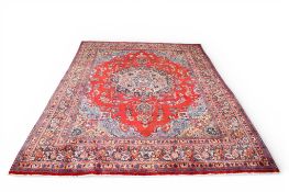 A large Persian rug on a red ground. Heavily decorated blue, green and pink pattern.