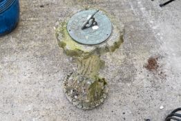 A patinated metal garden sundial on a composite stone pedestal with tree trucnk effect.