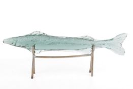 A decorative pale green, stylised glass fish on stand.
