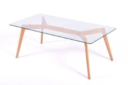 A modern glass top coffee table on light oak angled supports. Small chip to corner of glass.