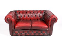 A 20th century ox blood red Chesterfield two seater sofa. Button-back, on castors.