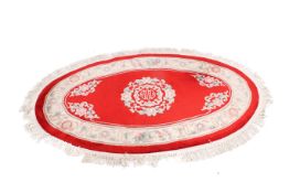 A Chinese style oval wool rug on a red ground. Having floral border and central motif.