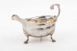 A George II silver sauce boat. With shaped rim, leaf scroll handle, raised on three hoof feet.