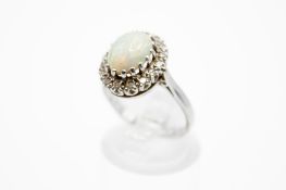 A white metal opal and diamond cluster ring. Set centrally with an oval cabochon cut opal of 1.