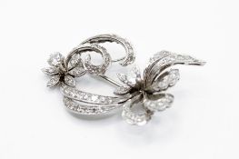 A white gold floriate scroll diamond set brooch. Set with two round brilliant cut diamonds of 0.