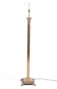 A brass standard lamp of Corinthian column form, over a square base and lion paw feet.