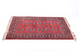 A red ground Bokhara rug with repeating medallions to the border and centre.