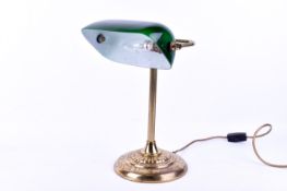 A brass bankers' desk lamp with green glass shade. Raised on a circular base.