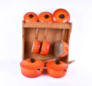 A set of five graduated Le Creuset orange enamel saucepans with wooden storage rack.