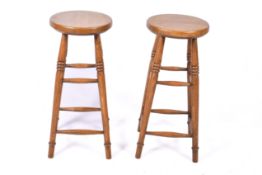 A pair of wooden bar stools stamped '44 - 90'. Having circular seats and stretchers.