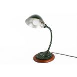 A circa 1930s industrial gooseneck desk lamp, painted dark green and raised on a wooden base.
