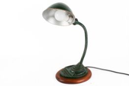 A circa 1930s industrial gooseneck desk lamp, painted dark green and raised on a wooden base.