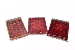 Three small assorted Afghan style wool rugs on red grounds.