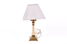A modern brass table lamp with shade. Raised on a square base.