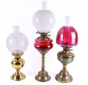 A group of three assorted brass oil lamps. Each with chimney and shade, raised on circular bases.