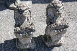 A pair of reconstituted stone lion garden statues holding shields. Raised on square bases.