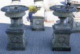 Pair of composition stone garden urns on plinths.