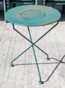A green metal garden table with decorative pierced top sat on three crisscross legs.