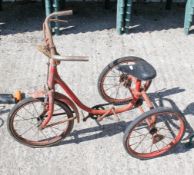 A vintage red tricycle in heavily worn condition. Pedals and chain turn wheels and brake functions.