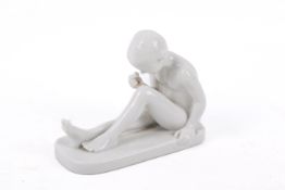 A white porcelain figure modelled as child seated on a rectangular plinth.