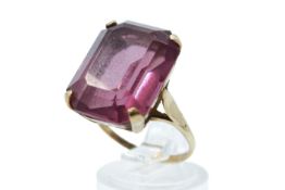 A yellow metal and purple stone dress ring. The faceted stone measuring 1.9cm x 1.