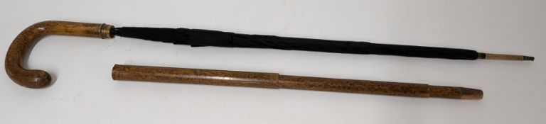 An umbrella stick, of black material, set within a sliding wood sheaf acting as a cane.