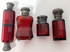 Four cranberry glass scent bottles, to include one of double ended design, white metal clasps, one