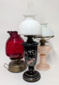 Three oil lamps, to include a cranberry glass example, pink glass, and decorated black example. (3)