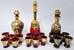 A collection of Murano red glass decanters and cups, with elaborate gilt and floral painted