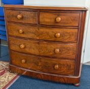 A Victorian flame mahogany bow front chest of drawers on bun feet with knob handles