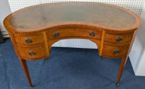 An Edwardian satinwood kidney shaped desk with green leather surface, tapered legs on casters