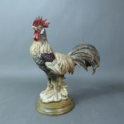 Continental figure of a rooster raised on a wooden circular base, overall height 26cm.
