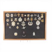 A collection of assorted British Army regimental cap badges, displayed on a black felt mount, to
