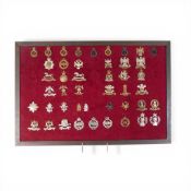 A collection of assorted British Army regimental cap badges, displayed on a red felt mount, to
