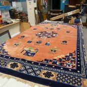 A large wool style Rug decorated with a navy pattered border with a floral central pattern on a