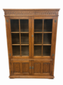 A Jacobean-style solid oak display cabinet with glazed upper doors and intricately carved lower pul