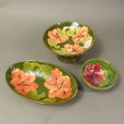 Moorcroft Hibiscus on green ground pattern items including footed bowl, oval dish & small bowl. (3)