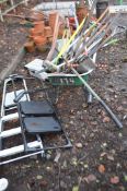 A WHEELBARROW CONTAINING GARDEN TOOLS AND STEP LADDERS including an oast shovel, clippers etc