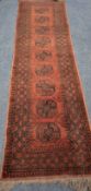 A RED GROUND RECTANGULAR WOOLLEN CARPET RUNNER, with nine Elephant foot motifs, surrounded by a