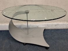 ROLF BENZ, AN OVAL GLASS TABLE, raised on a curved metal frame on castors, width 86cm x depth 50cm x