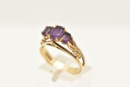 A 9CT GOLD AMETHYST RING, claw set with three oval cut amethysts, textured open work shoulders and