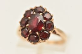 A 9CT GOLD GARNET CLUSTER RING, of an oval form, set with a central oval cut garnet centre within