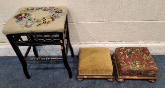 AN EARLY 20TH CENTURY EBONISED STOOL, with needlework upholstery, along with two footstools