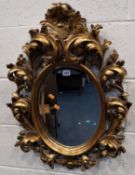 A REPRODUCTION GILT WOOD WALL MIRROR, with intricate foliate carved details surrounding an oval