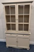 A CREAM PAINTED DRESSER, the double glass doors enclosing two shelves, atop a base with two