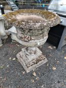 A 20TH CENTURY RED SANDSTONE GARDEN URN, depicting putto to facet, foliate detail, on a shaped