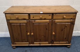 A MODERN PINE SIDEBOARD, fitted with three drawers over triple cupboard doors, raised on bun feet