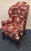 A LATE 19TH / EARLY 20TH CENTURY WINGBACK ARMCHAIR, with ruby red and foliate upholstery, outswept