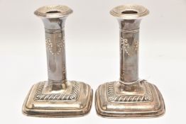 A PAIR OF EARLY 20TH CENTURY SILVER CANDLESTICKS, ribbon and swag pattern, on weighted square bases,